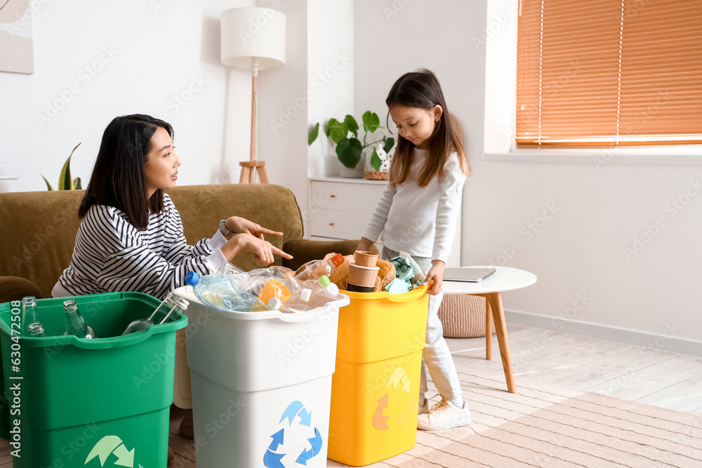 Asian mother with her little daughter sorting garbage in recycle bins at home