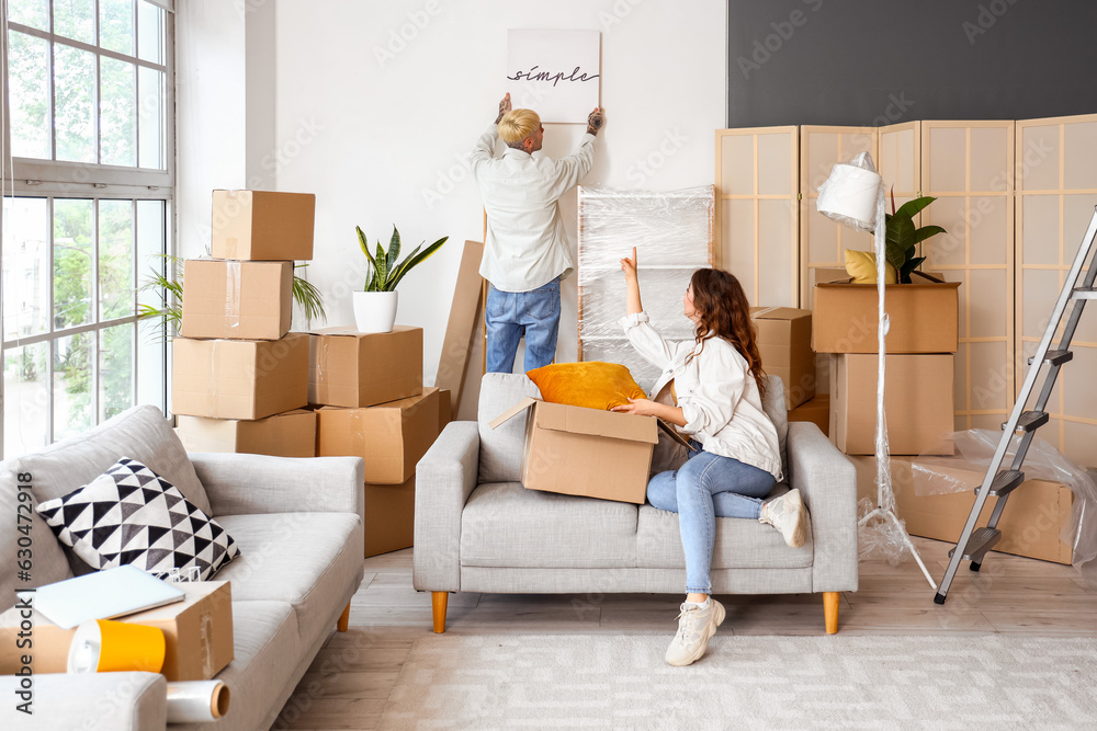 Young couple hanging poster in room on moving day