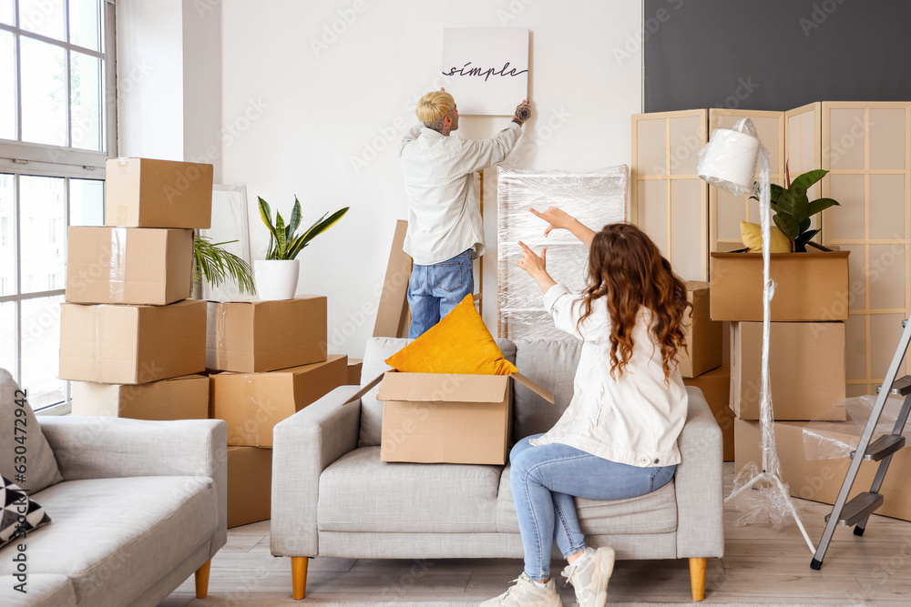 Young couple hanging poster in room on moving day