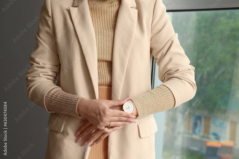 Young woman looking at wristwatch near window in room