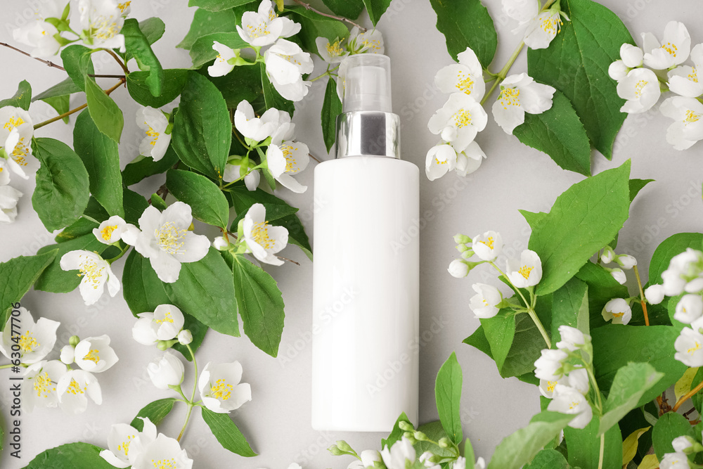 Composition with bottle of cosmetic product and beautiful jasmine flowers on light background