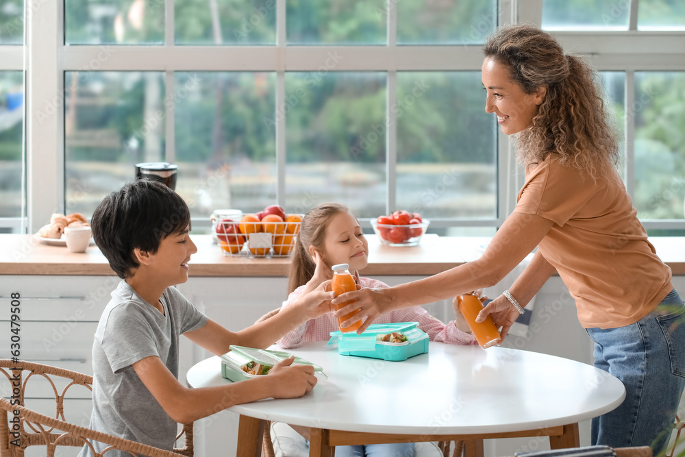 Mother giving bottles of juice to her little children in kitchen