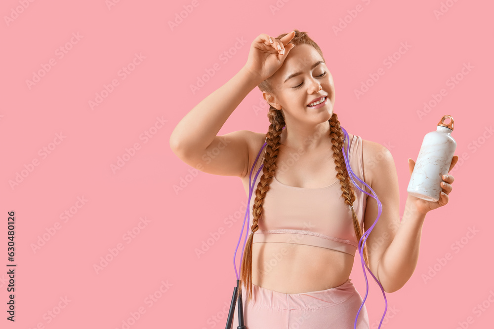 Sporty young woman with skipping rope and bottle of water on pink background