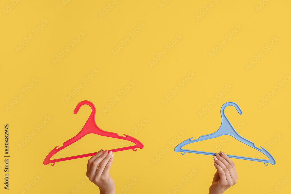 Woman holding plastic clothes hangers on yellow background