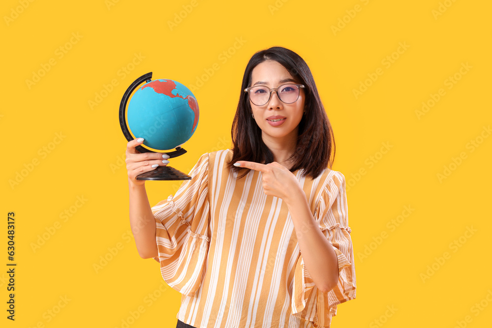 Female Asian Geography teacher with globe on yellow background