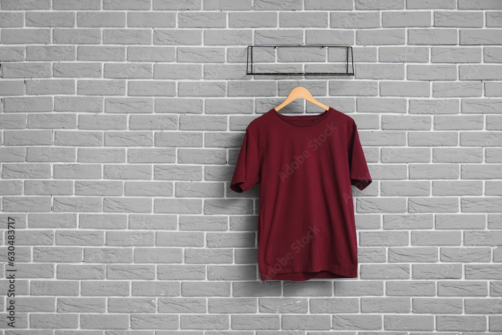 Stylish red t-shirt hanging on grey brick wall