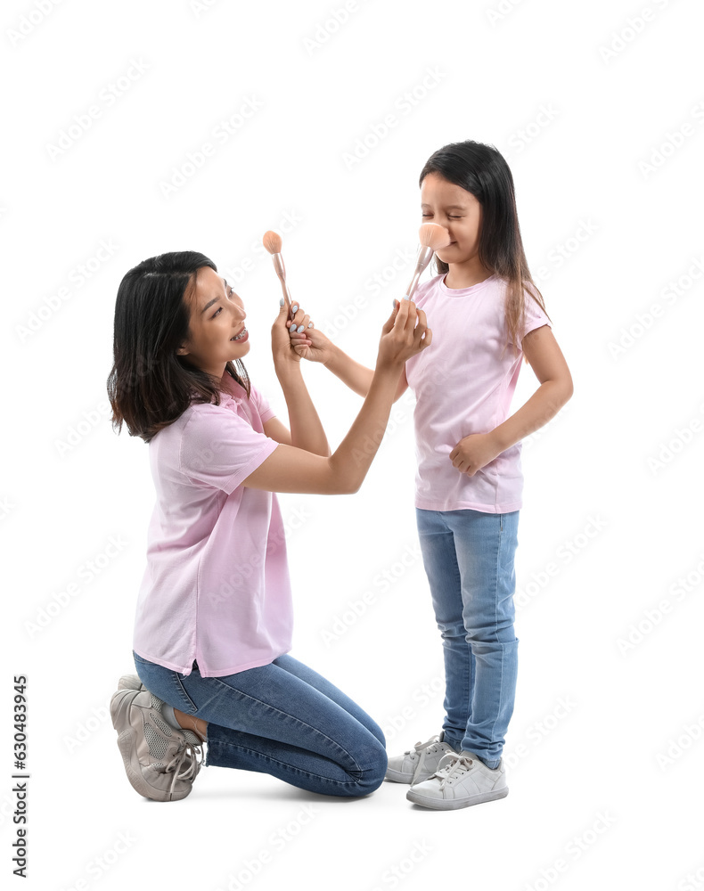 Asian mother with her little daughter and makeup brushes on white background