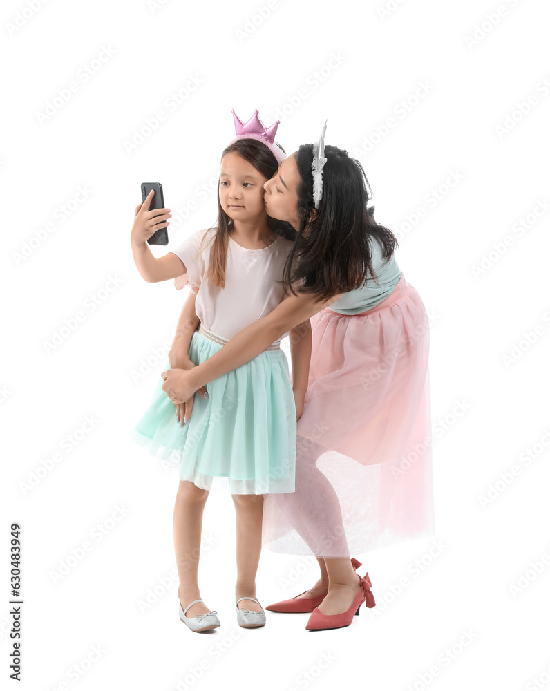 Asian mother with her little daughter in crowns taking selfie on white background