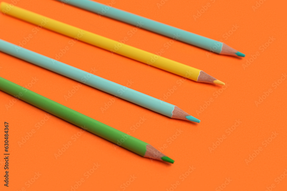 Different color pencils on orange background, closeup