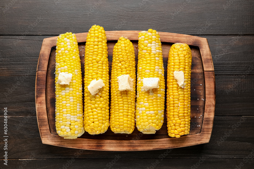 Board of boiled corn cobs with butter on wooden background