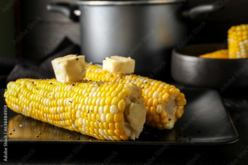 Plate of boiled corn cobs with butter on black background