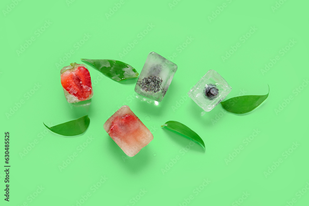 Frozen berries in ice cubes and leaves on green background