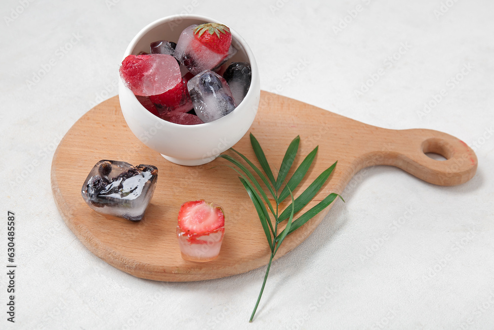 Bowl and wooden board with frozen berries in ice cubes on white background