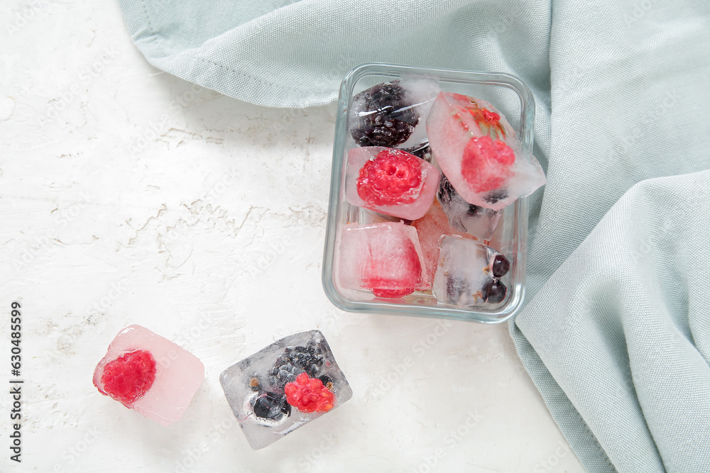 Glass bowl with frozen berries in ice cubes on white background