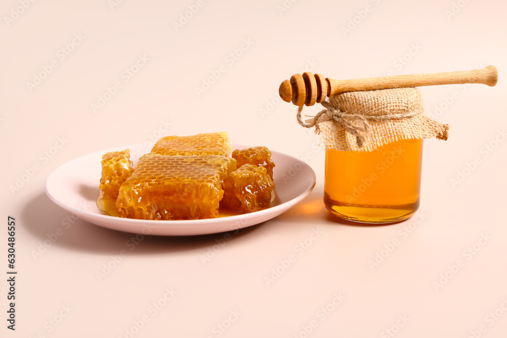 Jar of sweet honey and plate with combs on pink background