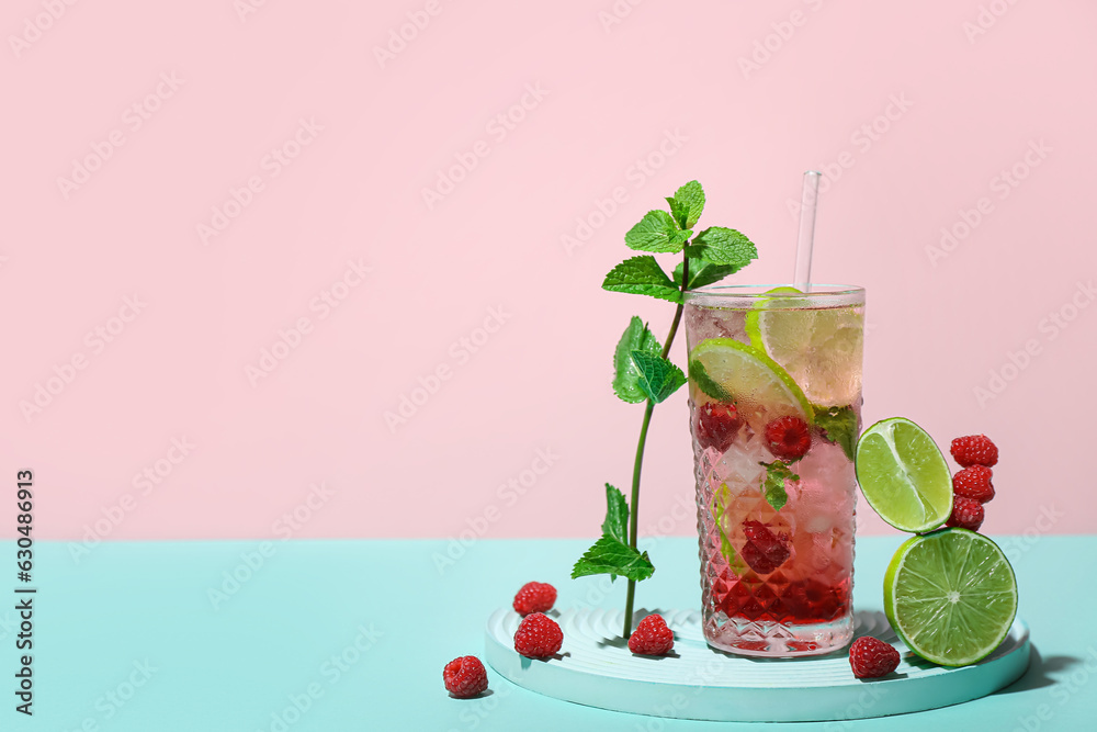 Glass of tasty raspberry mojito with lime and mint on color background