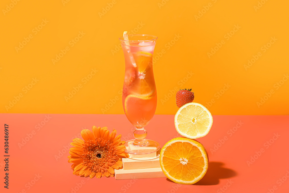 Glass of citrus cocktail with strawberry, lemon, orange and flower on color background