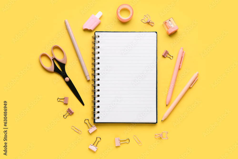 Notebook with different stationery supplies on yellow background