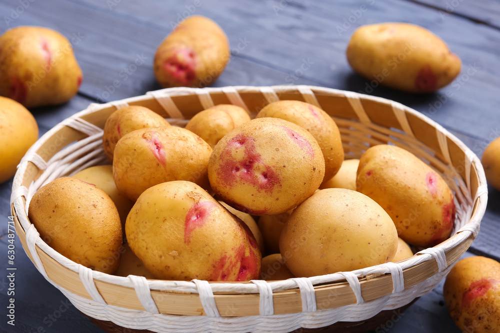 Wicker bowl with fresh raw potatoes on blue wooden background