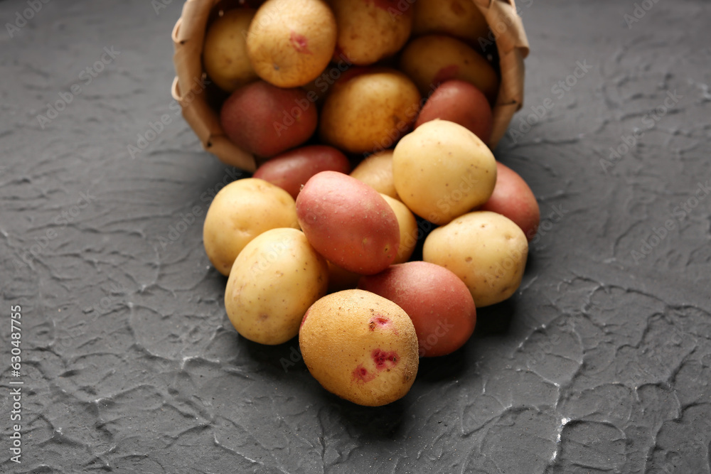 Wicker bowl with fresh raw potatoes on black background