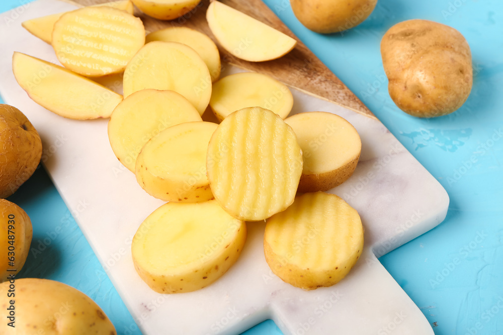 Board with slices of fresh raw potatoes on blue background