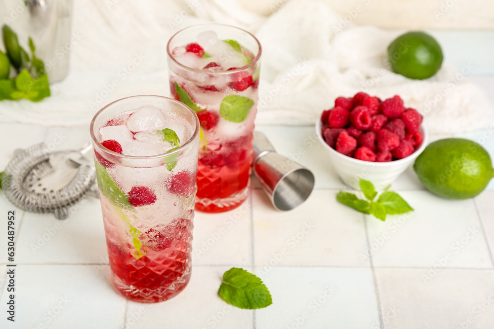 Glasses of fresh raspberry mojito and bowl with berries on white tile table