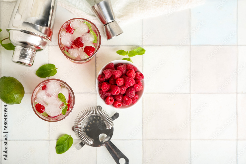 Glasses of fresh raspberry mojito and bowl with berries on white tile table