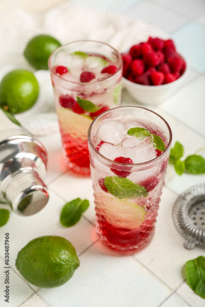 Glasses of fresh raspberry mojito and bowl with berries on white tile table