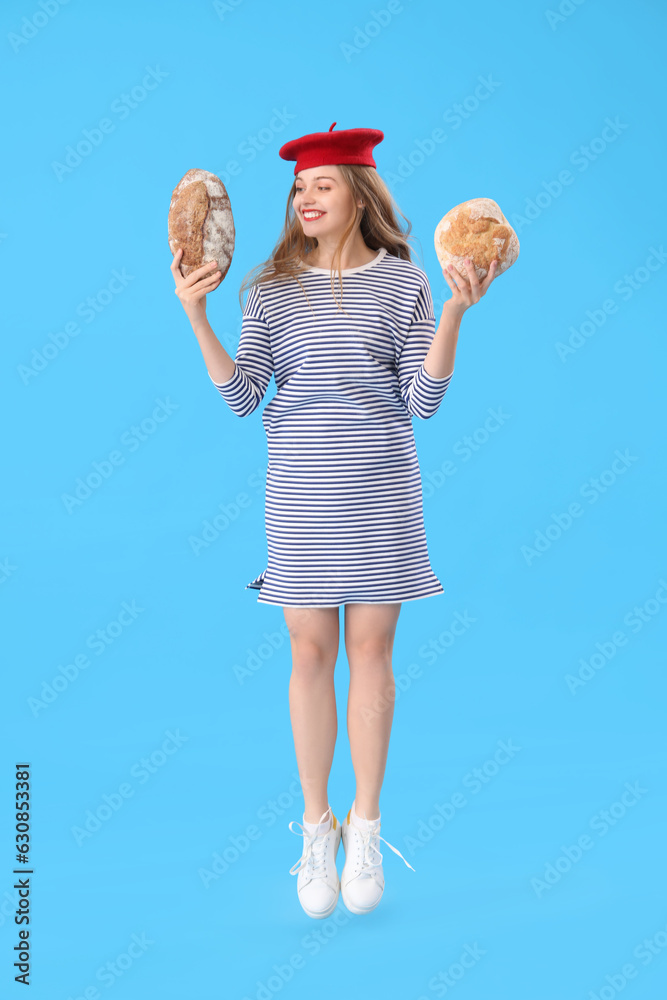 Young woman in beret with loaves of fresh bread jumping on blue background