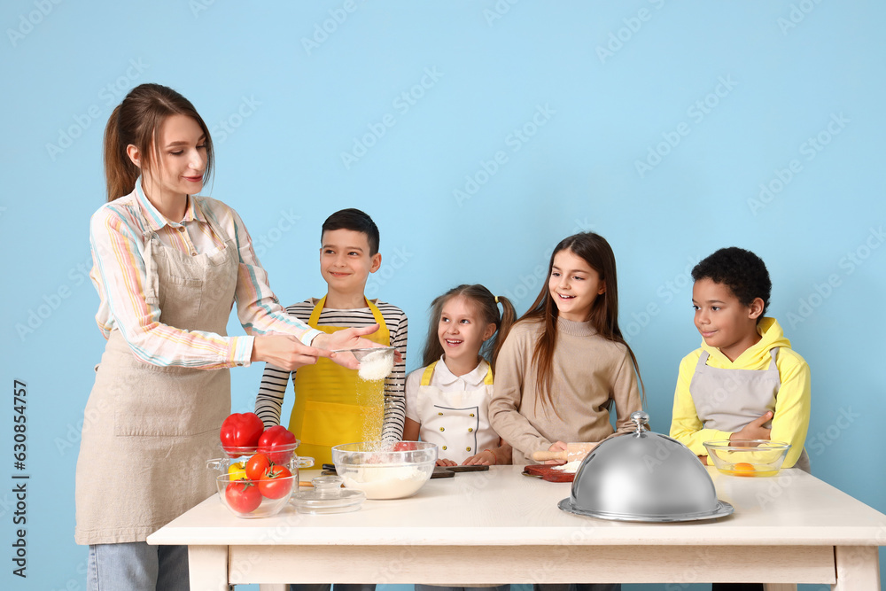 Female chef with group of little children during cooking class on blue background