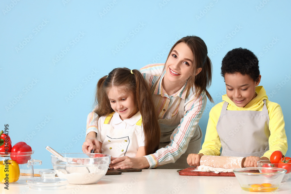 Female chef with little children during cooking class on blue background