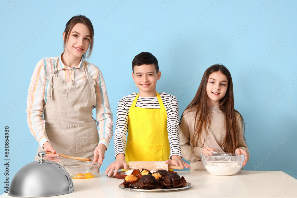 Female chef with little children during cooking class on blue background