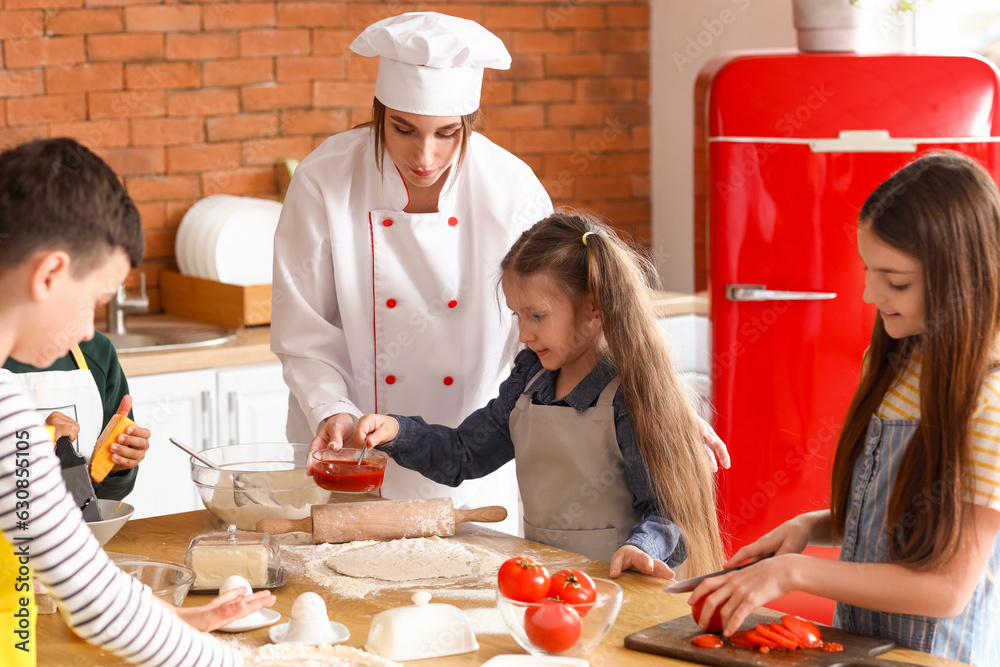 Female chef with group of little children preparing pizza during cooking class in kitchen