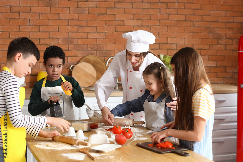 Female chef with group of little children preparing pizza during cooking class in kitchen