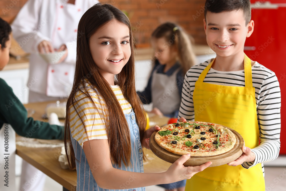 Little children with prepared pizza after cooking class in kitchen