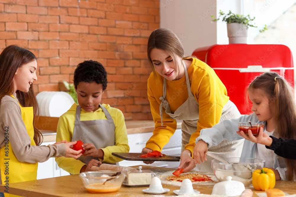 Female chef with group of little children preparing pizza during cooking class in kitchen