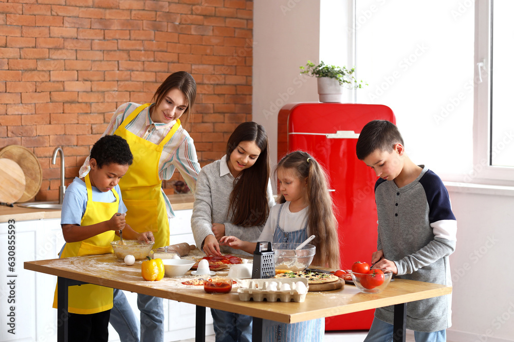 Female chef with group of little children preparing pizza during cooking class in kitchen