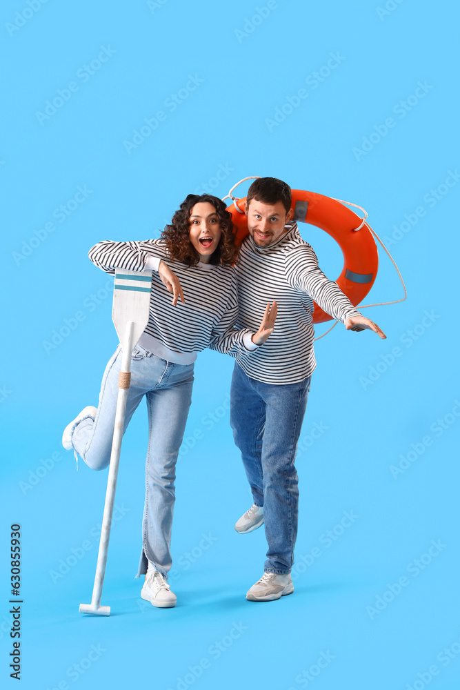 Young couple with paddle and ring buoy on blue background