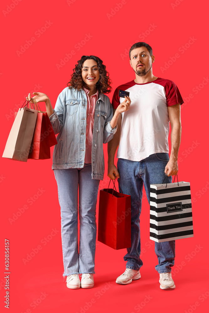 Young couple with shopping bags on red background