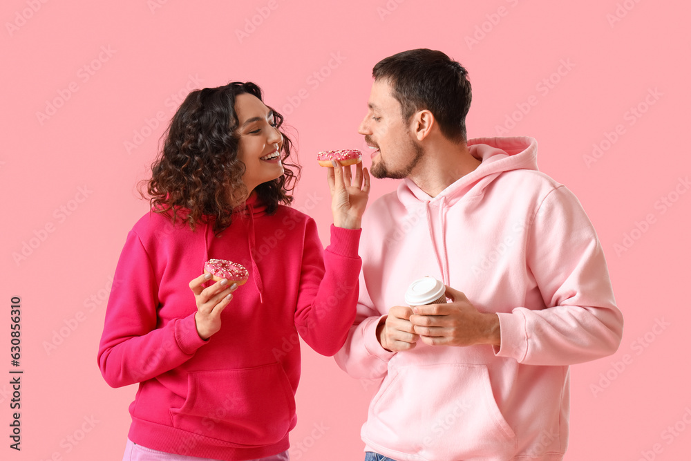 Young couple with tasty donuts and cup of coffee on pink background