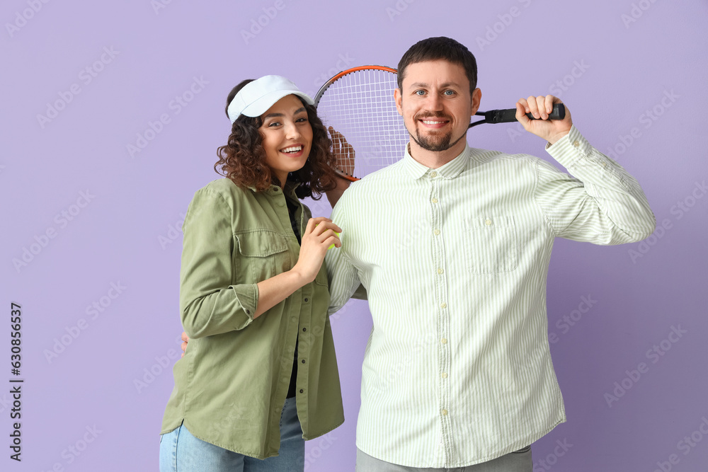 Young couple with tennis racket and ball on lilac background