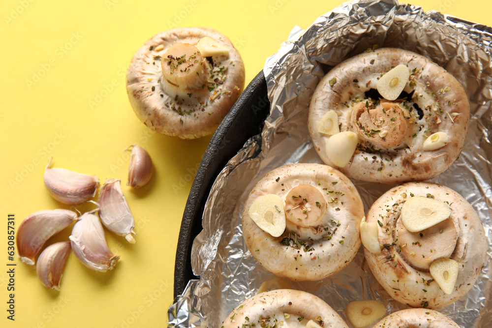 Baking dish with raw mushrooms, spices and garlic on yellow background, closeup