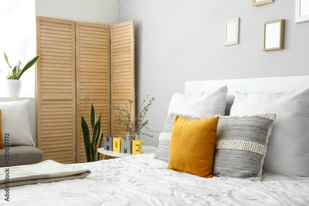 Cozy bed with many pillows and blooming tree branches on bedside table