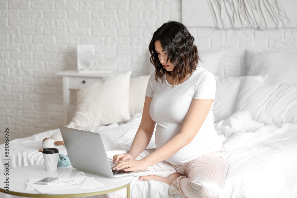 Young pregnant woman working with laptop in bedroom