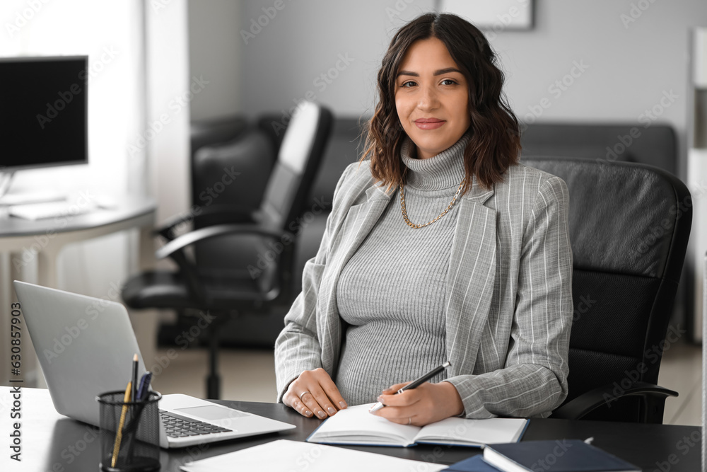 Young pregnant woman working at table in office