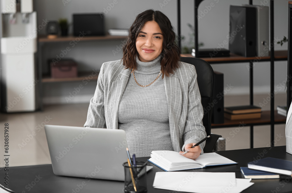 Young pregnant woman working at table in office