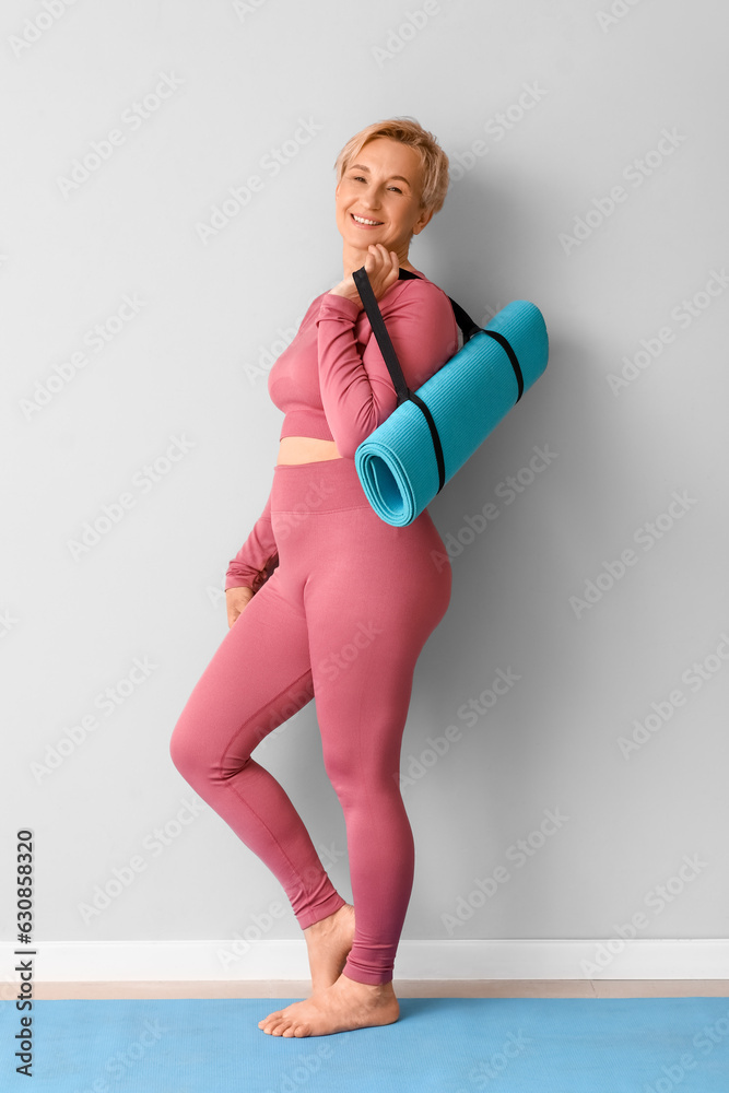 Mature woman with yoga mat near light wall