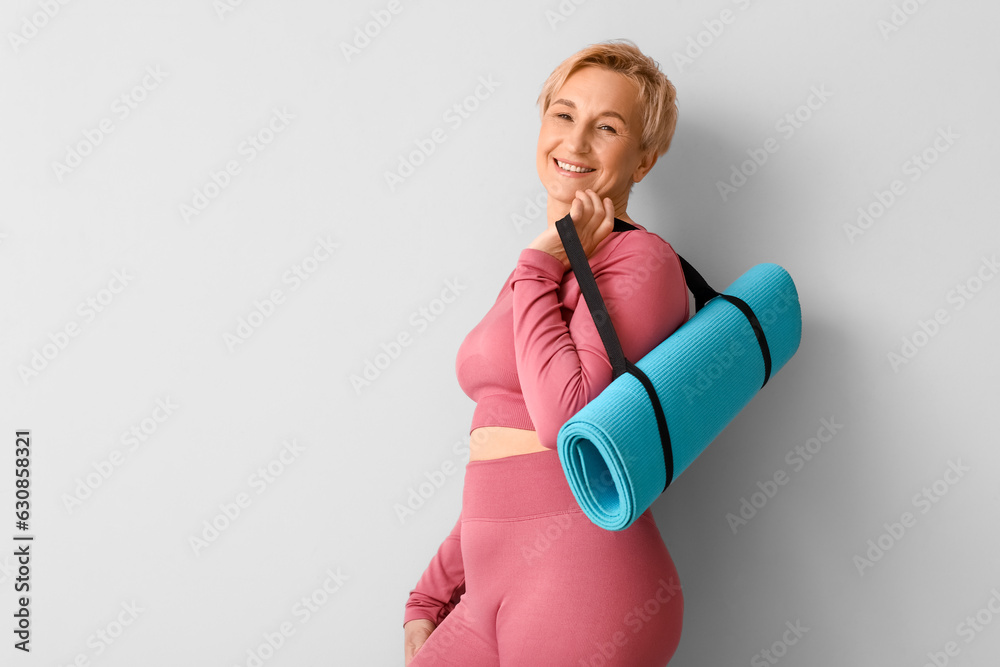 Mature woman with yoga mat on light background