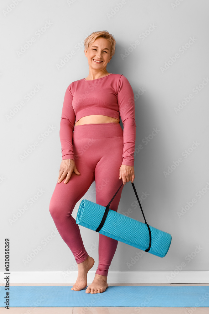 Mature woman with yoga mat near light wall