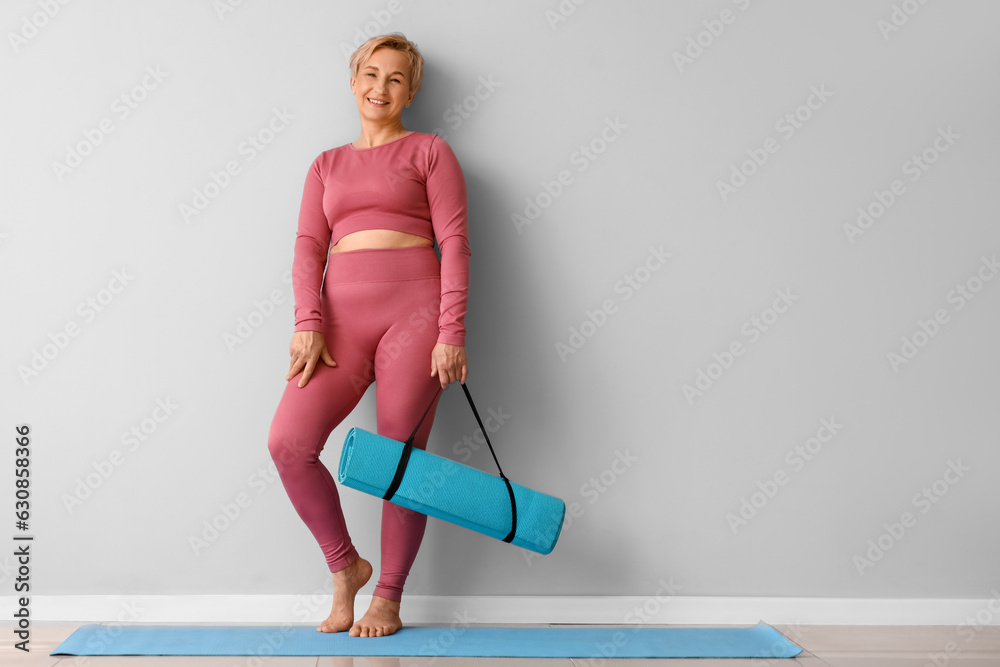 Mature woman with yoga mat near light wall